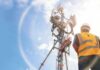Telecom tower with worker in safety vest under bright sky