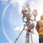 Telecom tower with worker in safety vest under bright sky
