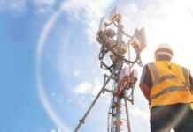 Telecom tower with worker in safety vest under bright sky