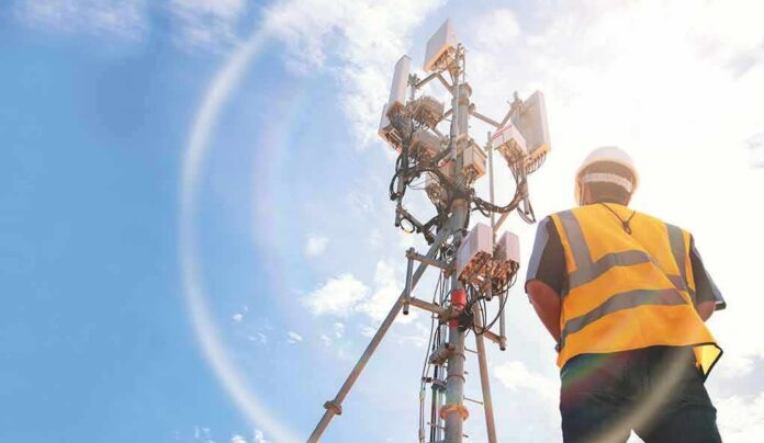 Telecom tower with worker in safety vest under bright sky