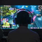 Gamer wearing headphones facing a large screen