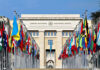 Backroom Talks Amid Annihilation Threats United Nations building with numerous national flags outside.