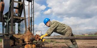 Worker in blue hard hat operating rusty oil pump equipment outdoors