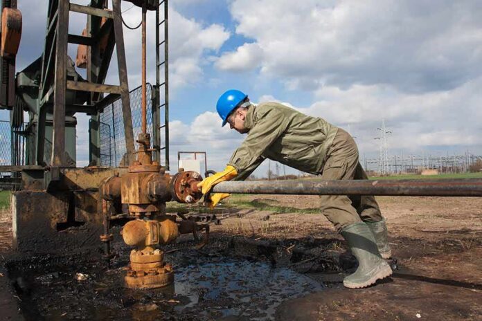 Worker in blue hard hat operating rusty oil pump equipment outdoors