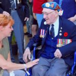 Elderly veteran in wheelchair greeted by woman