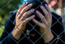 Person behind chain-link fence holding head in hands