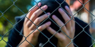 Person behind chain-link fence holding head in hands