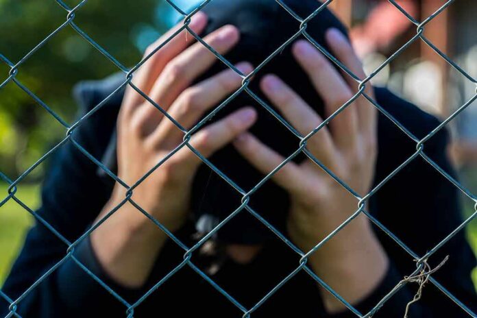 Person behind chain-link fence holding head in hands