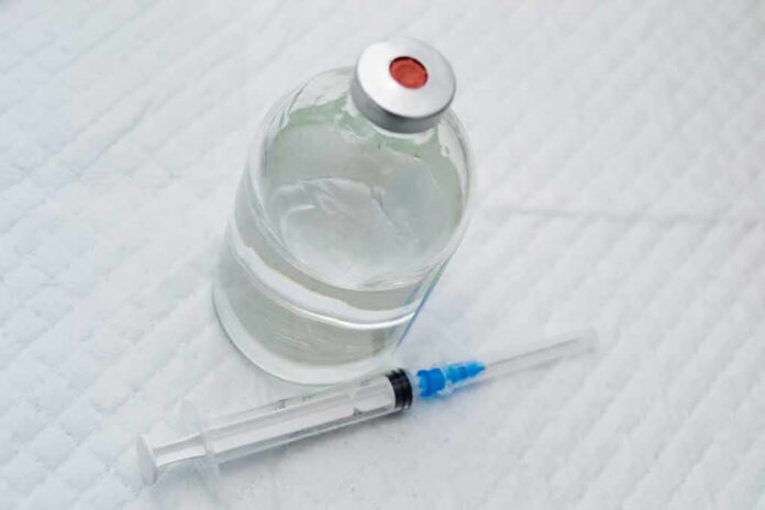 Vial of clear liquid with syringe on a white surface