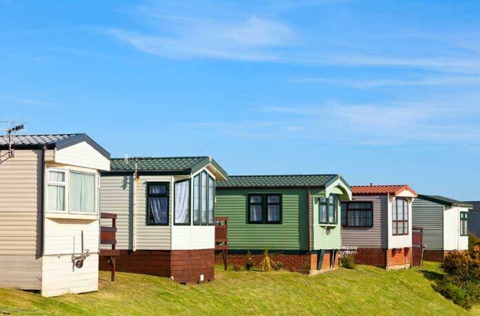 Row of colorful mobile homes on a grassy hill under a blue sky