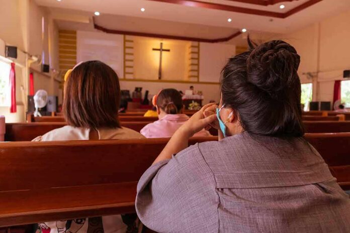 people seated in church pews facing a cross