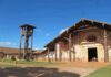 Wooden mission church with ornate facade and separate bell tower under blue sky