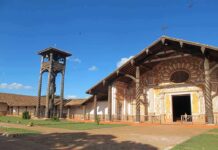 Wooden mission church with ornate facade and separate bell tower under blue sky