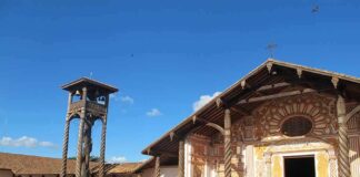 Wooden mission church with ornate facade and separate bell tower under blue sky