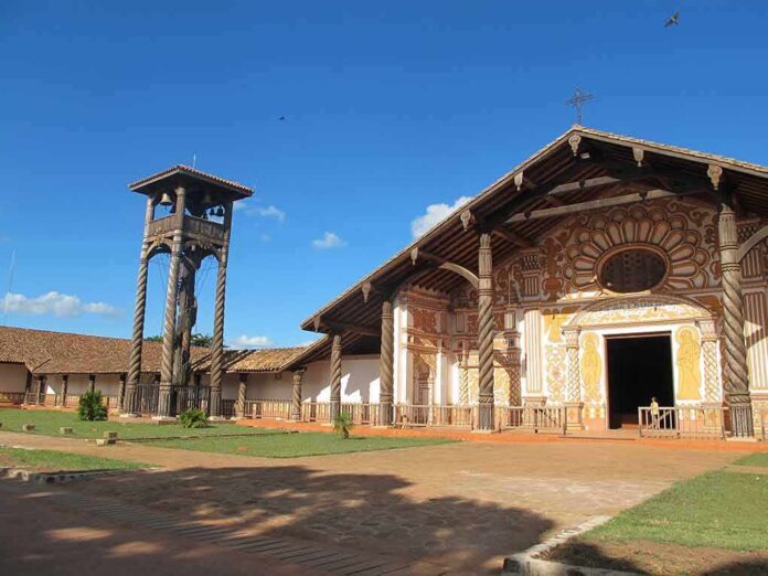 Wooden mission church with ornate facade and separate bell tower under blue sky