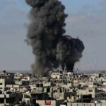 Thick black smoke rises from an explosion over a dense urban area