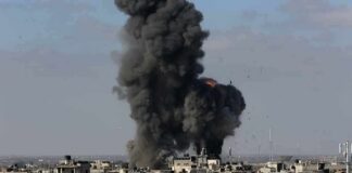 Thick black smoke rises from an explosion over a dense urban area
