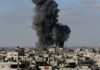 Thick black smoke rises from an explosion over a dense urban area