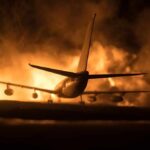 Airplane on runway with large fire and smoke at night