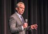 man in a suit speaking into a microphone on stage