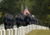 Military honor guard marches through a cemetery with flags