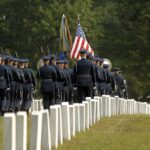 Military honor guard marches through a cemetery with flags