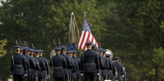 Military honor guard marches through a cemetery with flags