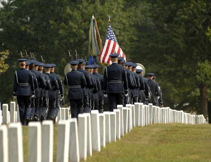 Military honor guard marches through a cemetery with flags
