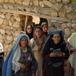 Group of women in traditional clothing standing in front of a stone wall