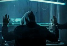 Hooded person at computer raises hands as another clamps handcuffs