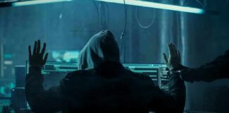 Hooded person at computer raises hands as another clamps handcuffs