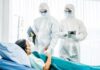 Medical staff in hazmat suits attend to a patient in a hospital bed