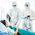 Medical staff in hazmat suits attend to a patient in a hospital bed