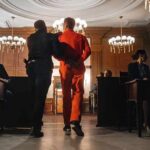 Prisoner in orange jumpsuit escorted by officer in a courtroom
