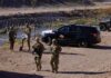 Soldiers stand near barbed wire beside a police SUV