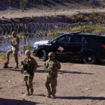 Soldiers stand near barbed wire beside a police SUV