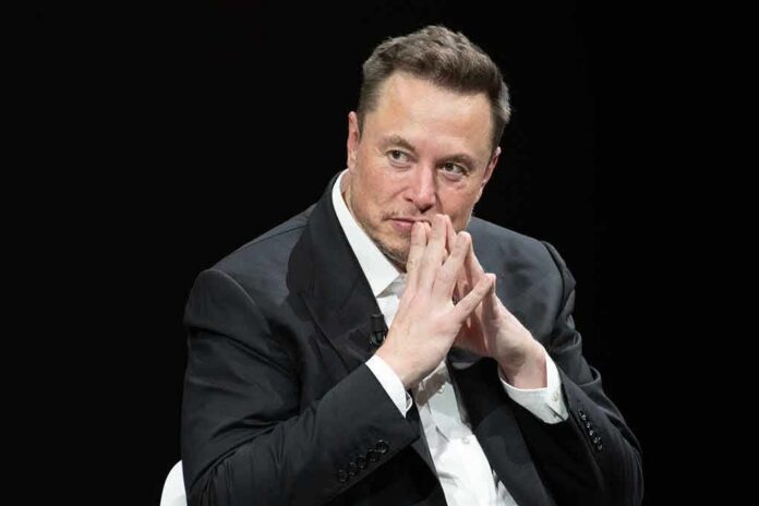 Elon Musk seated in a dark setting with hands steepled near his face