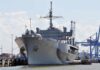 Navy’s $300M Robot Bet Raises Eyebrows Large gray naval ship docked at an industrial port