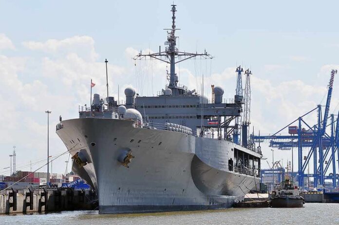 shutterstock_452352514-1 Large gray naval ship docked at an industrial port