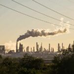 Industrial refinery with smokestack emitting plume at sunset