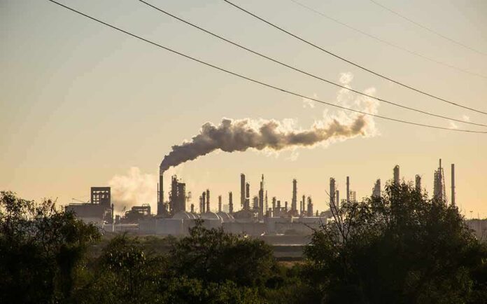Industrial refinery with smokestack emitting plume at sunset